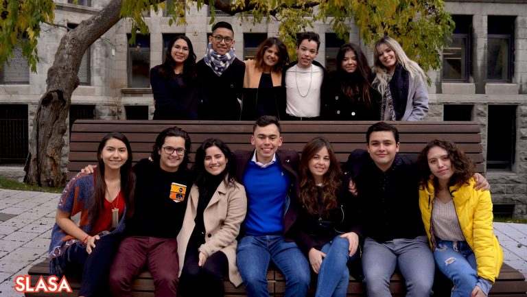 Image of 13 individuals half of which are on a bench the other half who are standing posing for the photo